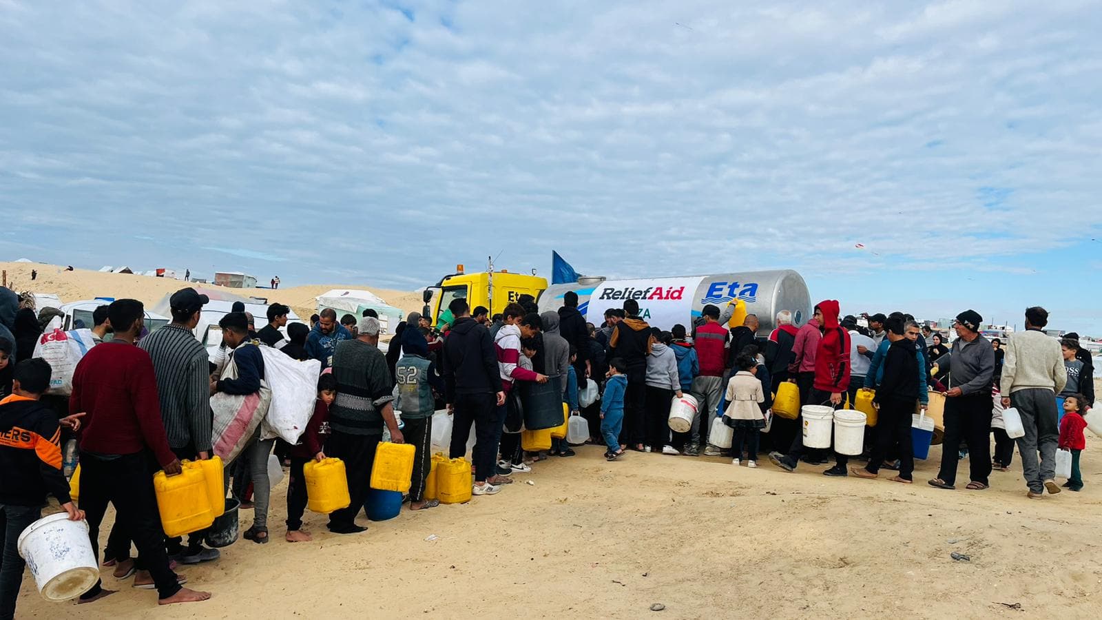 A large group holding buckets line up for a ReliefAid water truck